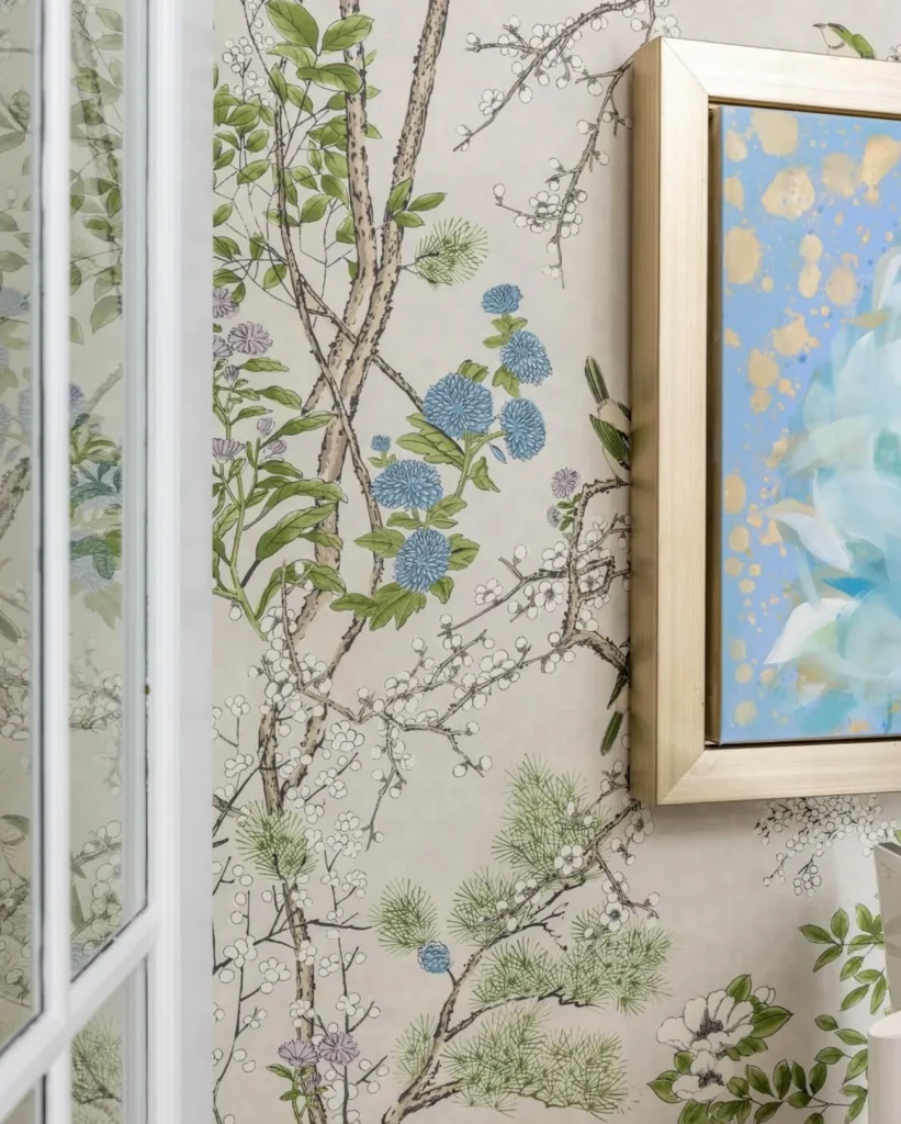 Floral wallpaper with branches and blue flowers next to a framed painting featuring abstract blue and gold patterns.